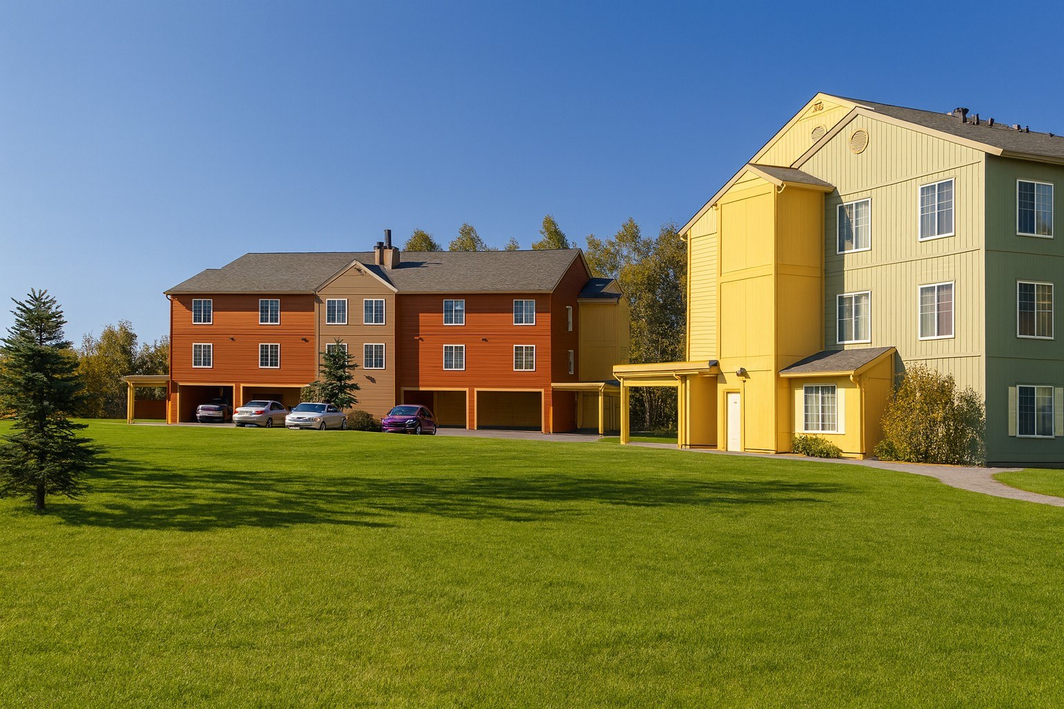 A large building with a yellow section is surrounded by a green lawn.